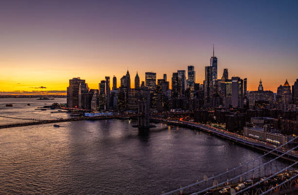 lower manhattan skyscrapers silhouettes against colourful sunset sky. heavy traffic on roads along water. manhattan, new york city, usa - new york city night brooklyn bridge skyline imagens e fotografias de stock