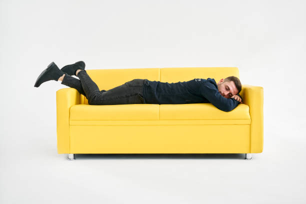istock Tired young man lying down on yellow sofa over white background 1405848994
