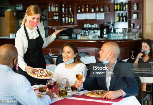 Waitress In Mask Serving Cheerful People In Pizzeria Stock Photo - Download Image Now