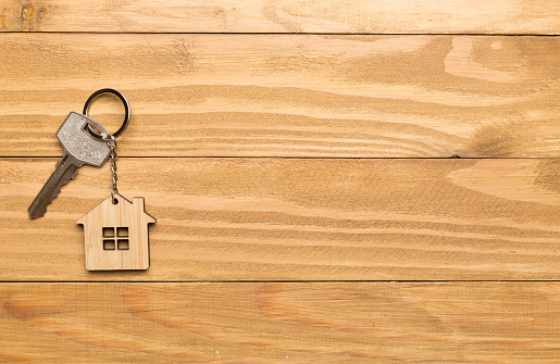 Keys with house-shaped keychain on wooden background.
