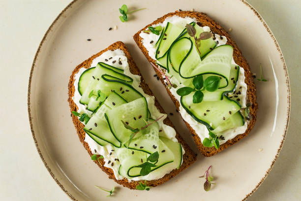 Breakfast, cereal bread sandwiches, cream cheese, sliced cucumber, with micro greenery on a light table, close-up, top view, selective focus, no people,