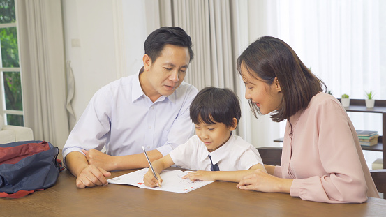 Portrait of happy smiling Asian Family. A student studying homework from school at home or house in family relationship. Love of father, mother, and son. People lifestyle. Education activity.