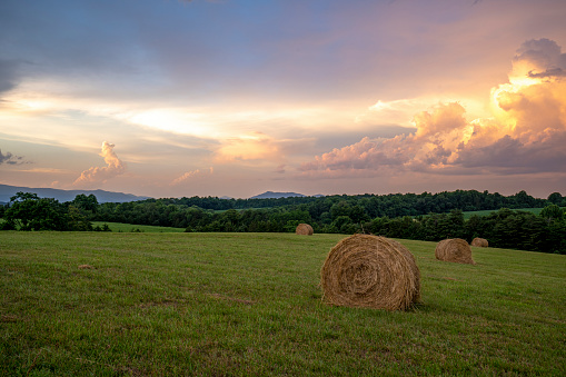 Vibrant sunset over a field of hay bales with the Blue Ridge Mountains in the background in rural small town Virginia, USA