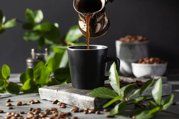 istock Coffee is poured into a black mug from a metal cup on a dark background. 1405856512