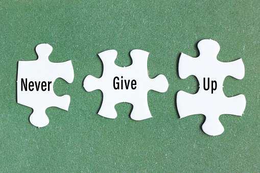 Motivational text on three pieces of white jigsaw puzzle on green background - Never give up.