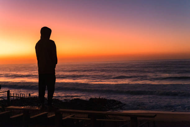 istock Beach Man Silhouetted Overlooking Ocean Sky Colors 1405857873
