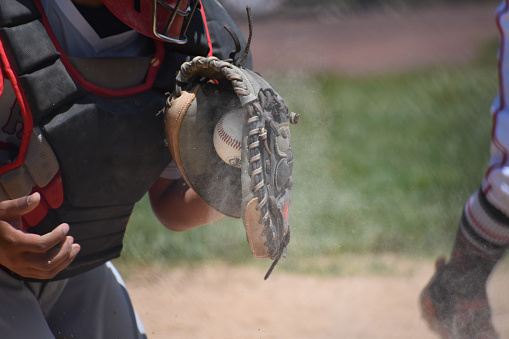 A baseball catcher holding up a leather glove on one knee on the pitch