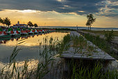 Wooden pier with a boat in the town of Podersdorf on Lake Neusiedl in Austria. In the background is a dramatic sunset sky.