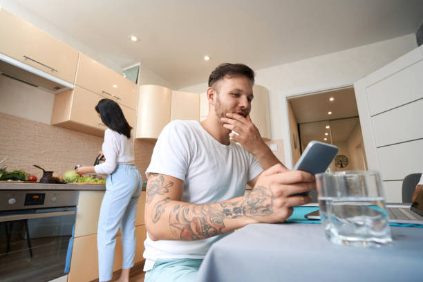 istock Male scrolling on his smartphone while wife cooking in kitchen 1405862174