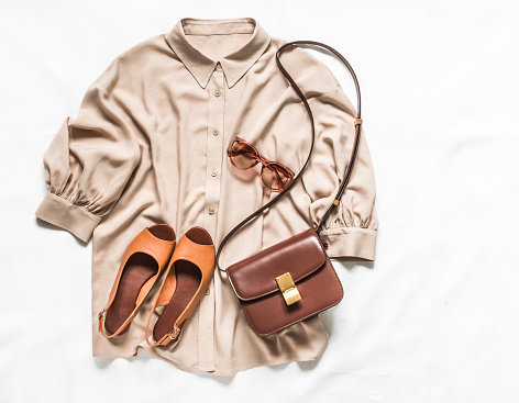 Women's blouse, leather sandals, cross body bag and sunglasses on a light background, top view