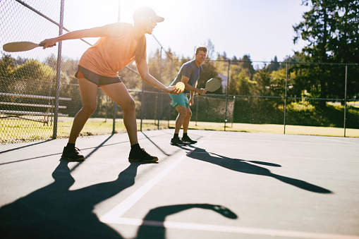 A youthful and fun Caucasian couple in their 50's enjoy the recreational sport of Pickleball on a warm day in the Pacific Northwest.  Shot in Washington state.