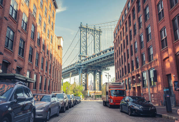манхэттенский мост между манхэттеном и бруклином через ист-ривер виден с узкого переулка, окруженного двумя кирпичными зданиями в солнечн� - brooklyn стоковые фото и изображения