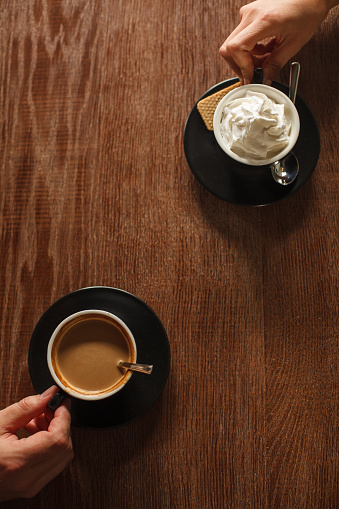 Directly above shot of two unrecognizable people, sitting opposite each other at the table at the cafe, holding their cups of coffee they are enjoying while hanging out.