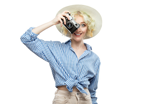 A beautiful, attractive female photographer in a blue plaid shirt and straw hat is holding a vintage camera. tourism and travel concept.