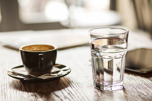 Close up shot of a glass of water and a cup of coffee served on a table at the coffee shop.