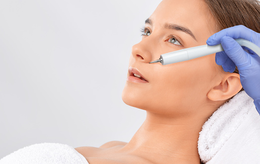 The cosmetologist makes the procedure treatment of Couperose of the facial skin of a beautiful, young woman in a beauty salon.Cosmetology and professional skin care.