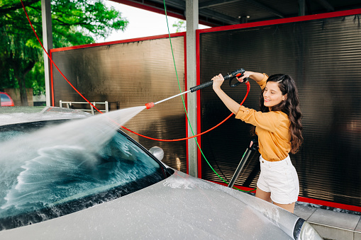 Shot of young woman washing her car outdoors