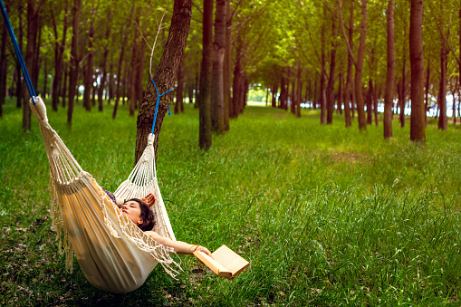 Young women having a relaxation moment in the forest by reading a book in the hammock