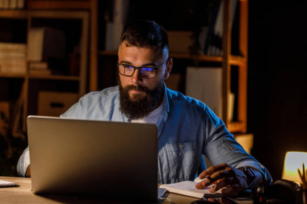 istock Young hipster businessman using laptop and writing in a notebook when working late at his desk 1405870245