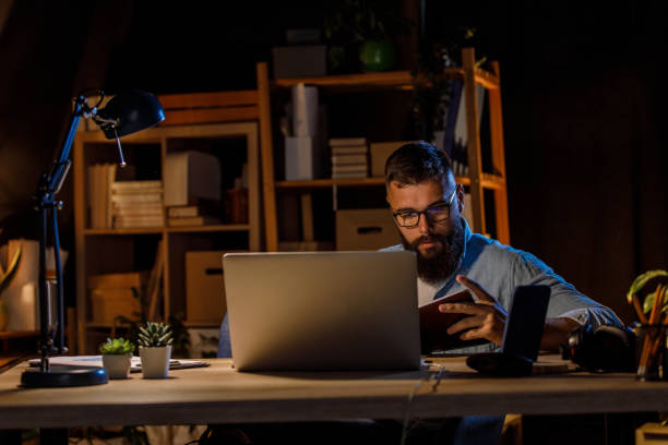 istock Young man reading notes in his notepad when working late at his desk 1405870261