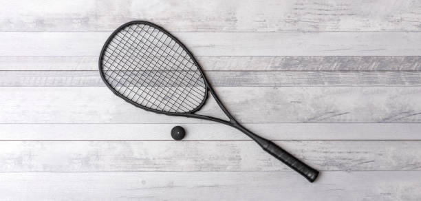 schwarzer squashschläger und ball auf grauem platz. horizontales sportthemenposter, grußkarten, header, website und app - squash racket stock-fotos und bilder