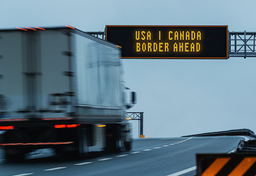 Semi truck approaching a border ahead highway sign. Composite image.