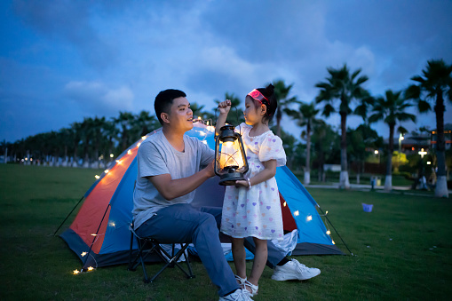 Father and daughter camping on the grass, lighting up the lights