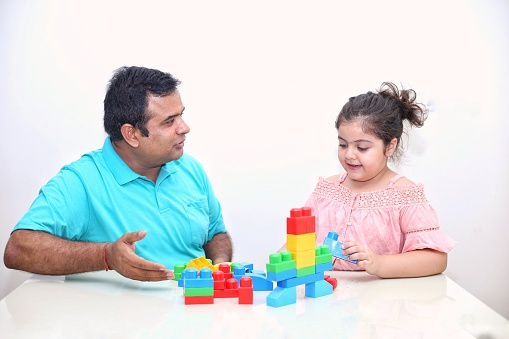 A young boy of Caucasian ethnicity is with his nanny, a female high school student of African ethnicity. They are spending time playing with blocks together.