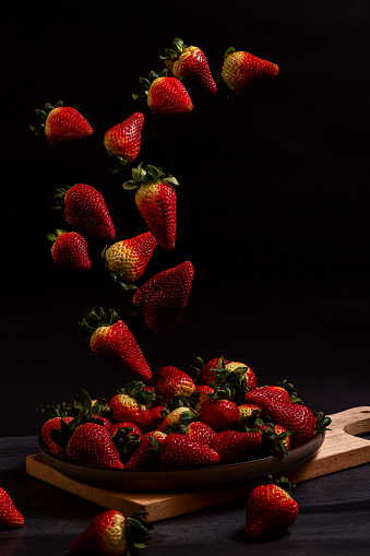 Strawberries falling into a plate on a wooden board