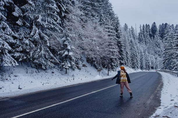 istock Woman on empty road through mountain forest with pines covered with snow 1405878148