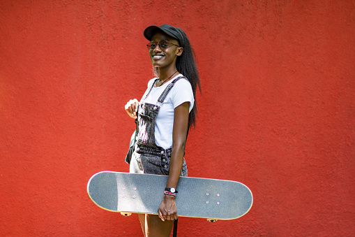 Young black woman portrait with skateboard against red wall
