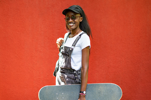 Young black woman portrait with skateboard against red wall
