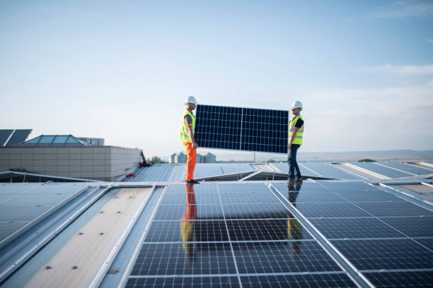 Workers installing photovoltaic system on a warehouse roof. stock photo