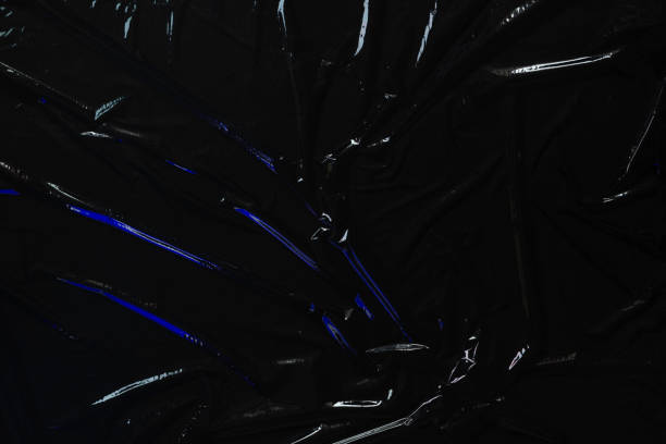 istock Transparent plastic wrap on black background. Crumpled wrinkled plastic cellophane. Reflecting blue color light and shadow on creases and folds in plastic surface. Texture overlay effect template 1405880376