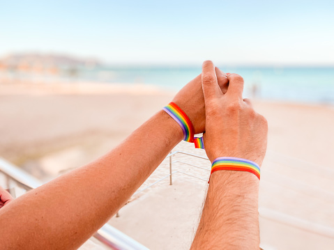 Hands intertwined with a bracelet with the colors of the rainbow of the LGTBI flag