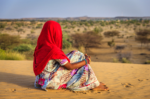 Gypsy Indian girl sitting on the sanddune and looking at the view, Rajasthan, India.