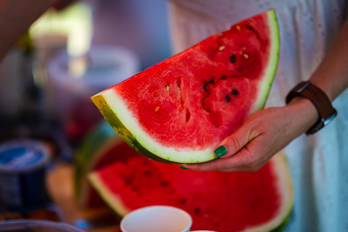 A piece of red juicy pitted watermelon is held by a young woman in her hand with a green manicure.