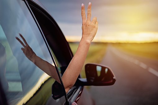 Woman is showing victory sign from her car on the road