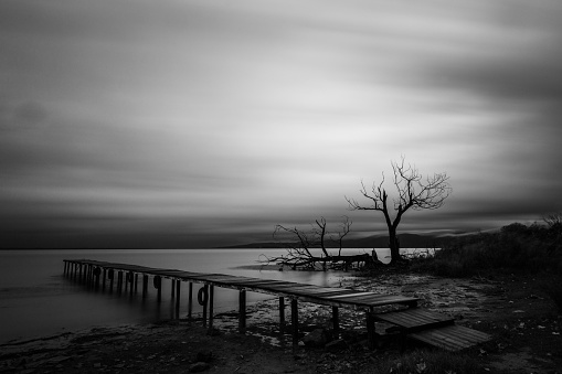 View of a pier on a lake at dusk, beneath a dramatic, moody sky.