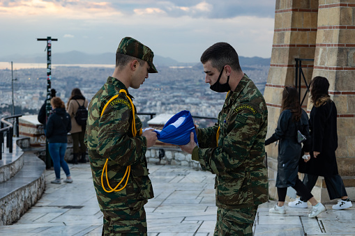 Two soldiers are lowering and folding the Greek flag at Mount Lycabettus