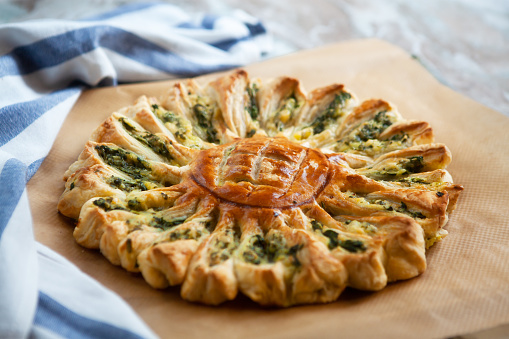 Delicious pie with spinach and ricotta cheese in the shape of a sunflower, towel next to it, close-up.