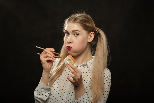 Cheerful blonde woman holding a bowl of vegetable salad and she is eating it.