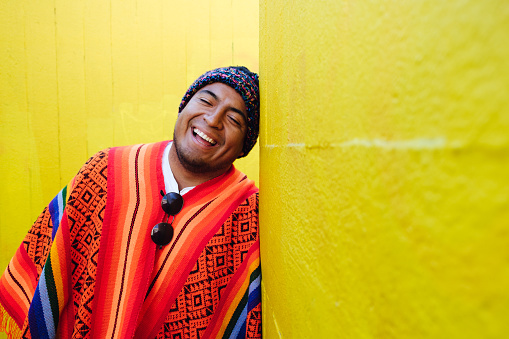 Young man with South American colorful poncho smiling in front of yellow wall