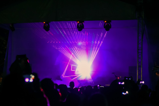 Purple laser neon beams. Crowd of people watching laser show at street festival. Many people enjoy the concert.