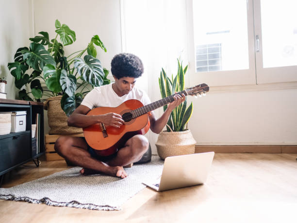 istock Afro man learning to play the guitar at home with a computer in online classes 1405896222