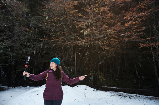 Hispanic woman is filming a video on her cell phone, while showing the native forest landscape. South America, Chile