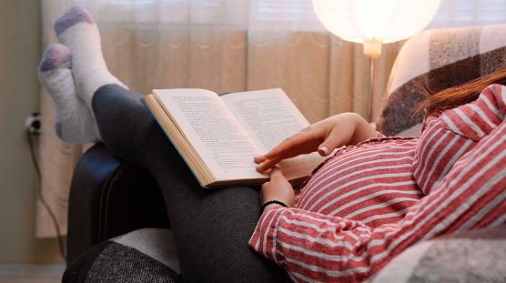 Relaxed woman is reading an interesting book in her leisure time while relaxing in the living room.