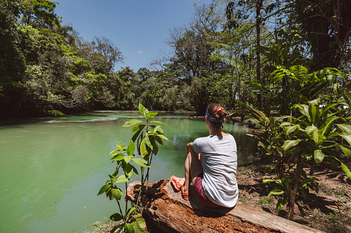 Woman sitting down enjoying a beautiful view of a river and lush tropical foliage.