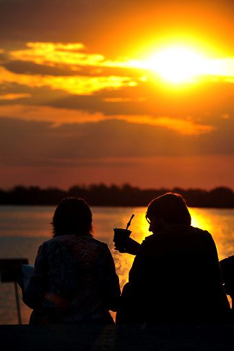 Porto Alegre, Rio Grande do Sul, Brazil - Aug 7th, 2015: View of sunset in Porto Alegre at Gasometro place. Silhouette of friends drinking yerba mate by Guaiba Lake