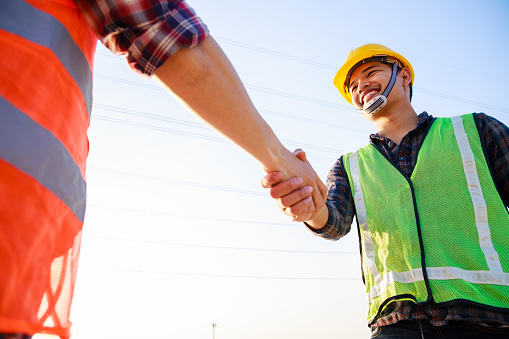 Two engineers shaking hands in construction site at the sunset. Business handshake concept.